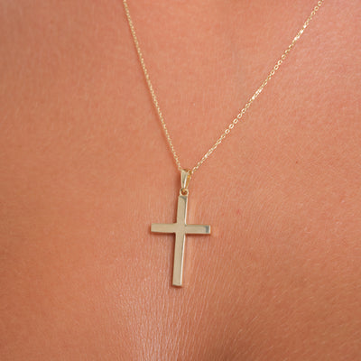 Gold cross necklace on a person's neck against a pink background