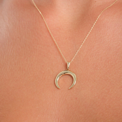 Gold crescent moon necklace on a person's neck against a pink background