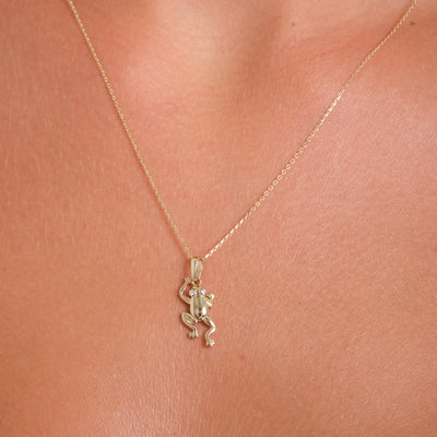 Gold necklace with a small pendant on a person's neck against a pink background