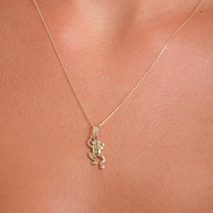 Gold necklace with a small pendant on a person's neck against a pink background