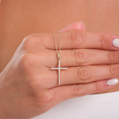 Gold cross necklace on a hand against a neutral background