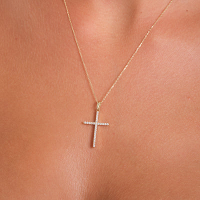 Gold cross necklace on a person's neck against a neutral background