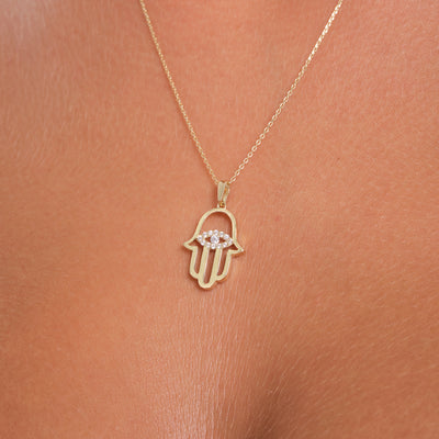 Gold Hamsa hand necklace with embedded stones on a skin-toned background