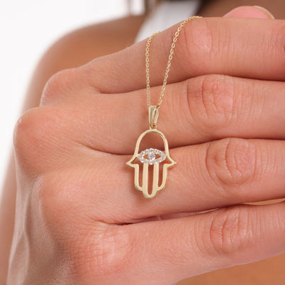 Gold Hamsa hand necklace with a diamond on a hand against a white background