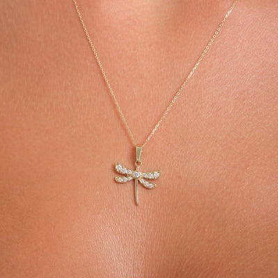 Gold dragonfly necklace on a person's neck against a neutral background