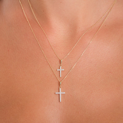 Two gold cross necklaces on a person's neck against a neutral background