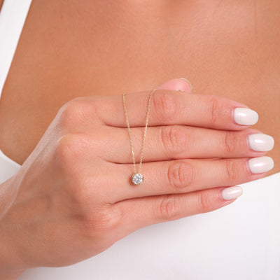 Hand wearing a delicate gold necklace with a small round pendant on a neutral background