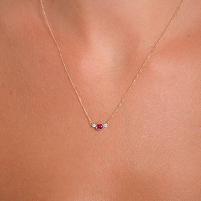 Gold necklace with a small red gemstone on a person's neck