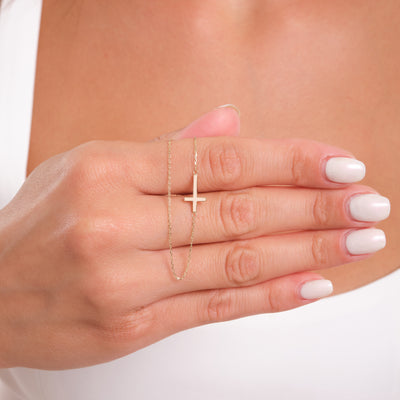 Hand wearing a gold cross necklace with a blurred background