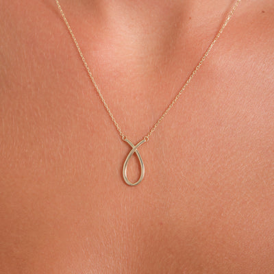 Gold infinity necklace on a person's neck against a neutral background