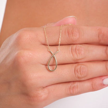Gold infinity necklace on a hand against a neutral background