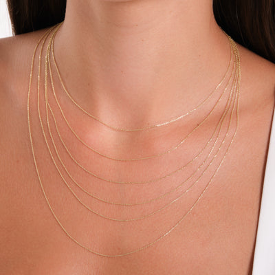 Close-up of a person wearing multiple thin gold necklaces on a plain background
