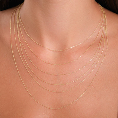 Close-up of a person wearing multiple thin gold necklaces on a plain background