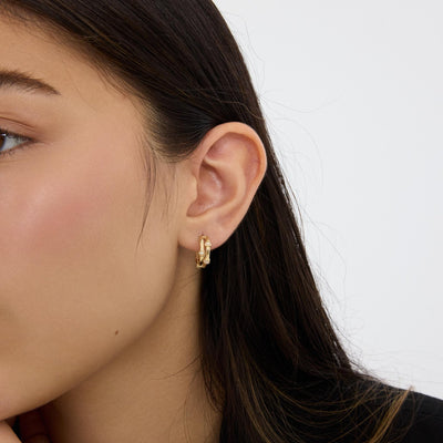 Close-up of 14K gold bamboo hoop earring with round cubic zirconia worn on the ear, long dark hair