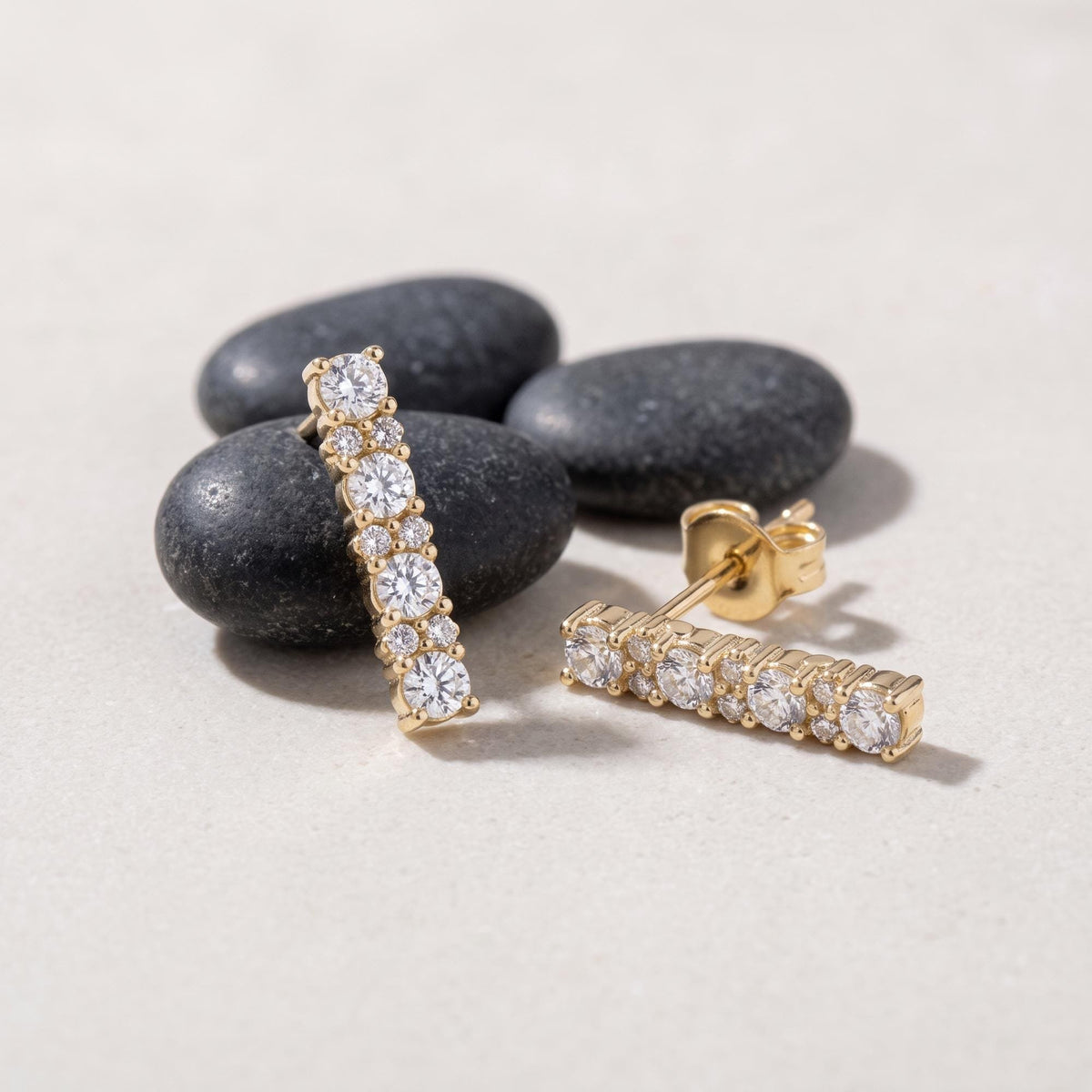 14K yellow gold bar stud earrings with cubic zirconia, pair resting on dark smooth stones