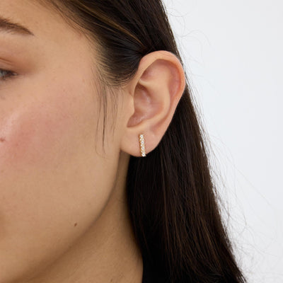 14K gold cubic zirconia bar stud earring worn in earlobe, close side view of model's ear