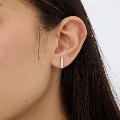 14K gold bar stud earring with cubic zirconia on ear, tight crop of vertical bar below the ear canal