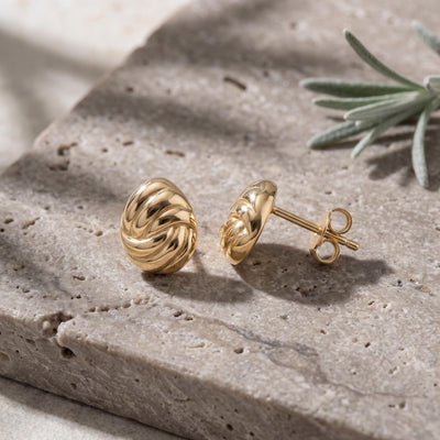 14K yellow gold braided knot stud earrings pair on a stone slab with a sprig of lavender, side view of post