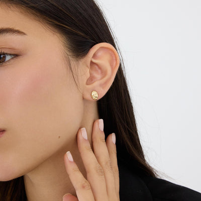 14K gold braided knot stud earring worn on ear, close-up with hand raised to the jaw