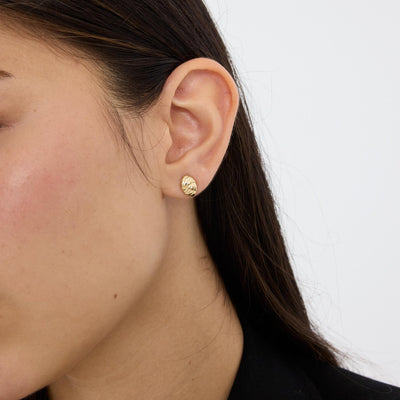 14K gold braided knot stud earring worn in earlobe, close side profile of ear against plain backdrop