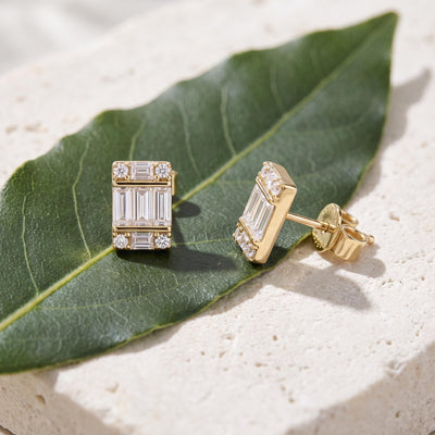 14K yellow gold cluster stud earrings with cubic zirconia, resting on a green leaf and stone slab