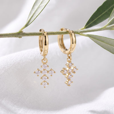14K yellow gold cross huggie earrings with cubic zirconia hanging from an olive branch over white fabric