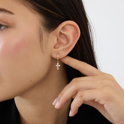 14K gold cross huggie earrings with cubic zirconia, held in a hand with the cross turned at an angle