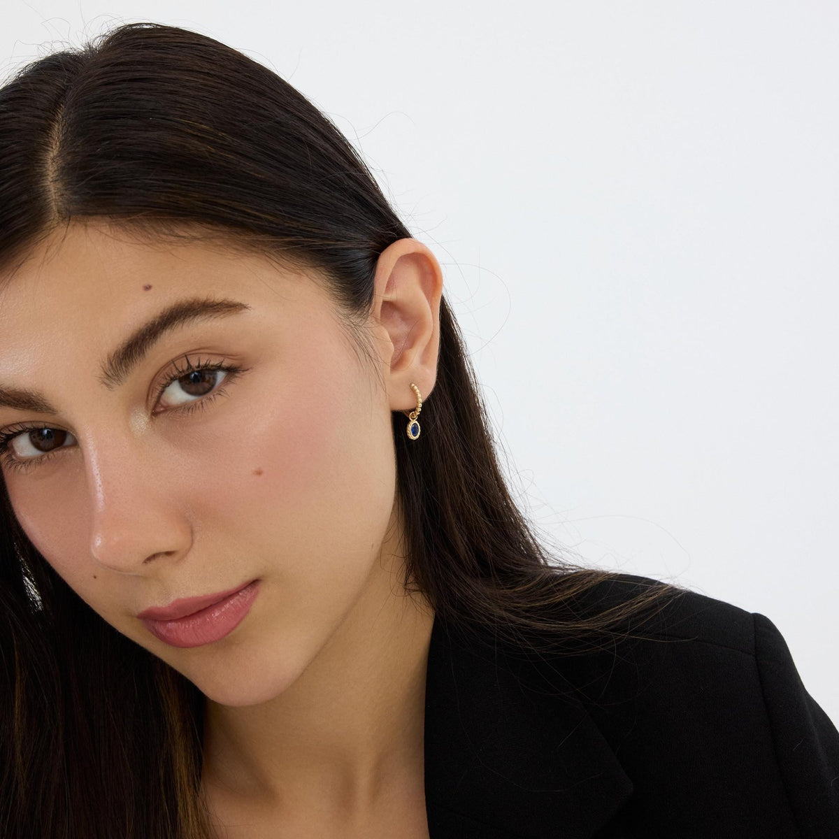 Model in black blazer wearing 14K gold beaded huggie earring with blue stone drop, close portrait