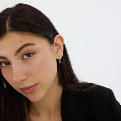 Model in black blazer wearing 14K gold beaded huggie earring with blue stone drop, close portrait