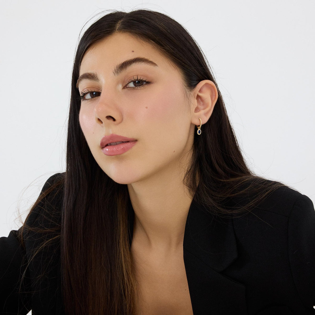 Model with long dark hair wearing 14K gold huggie earring with blue stone, shown at wider angle