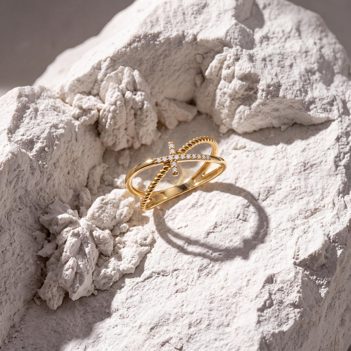 14K yellow gold CZ cross ring resting on rough white stone in soft daylight