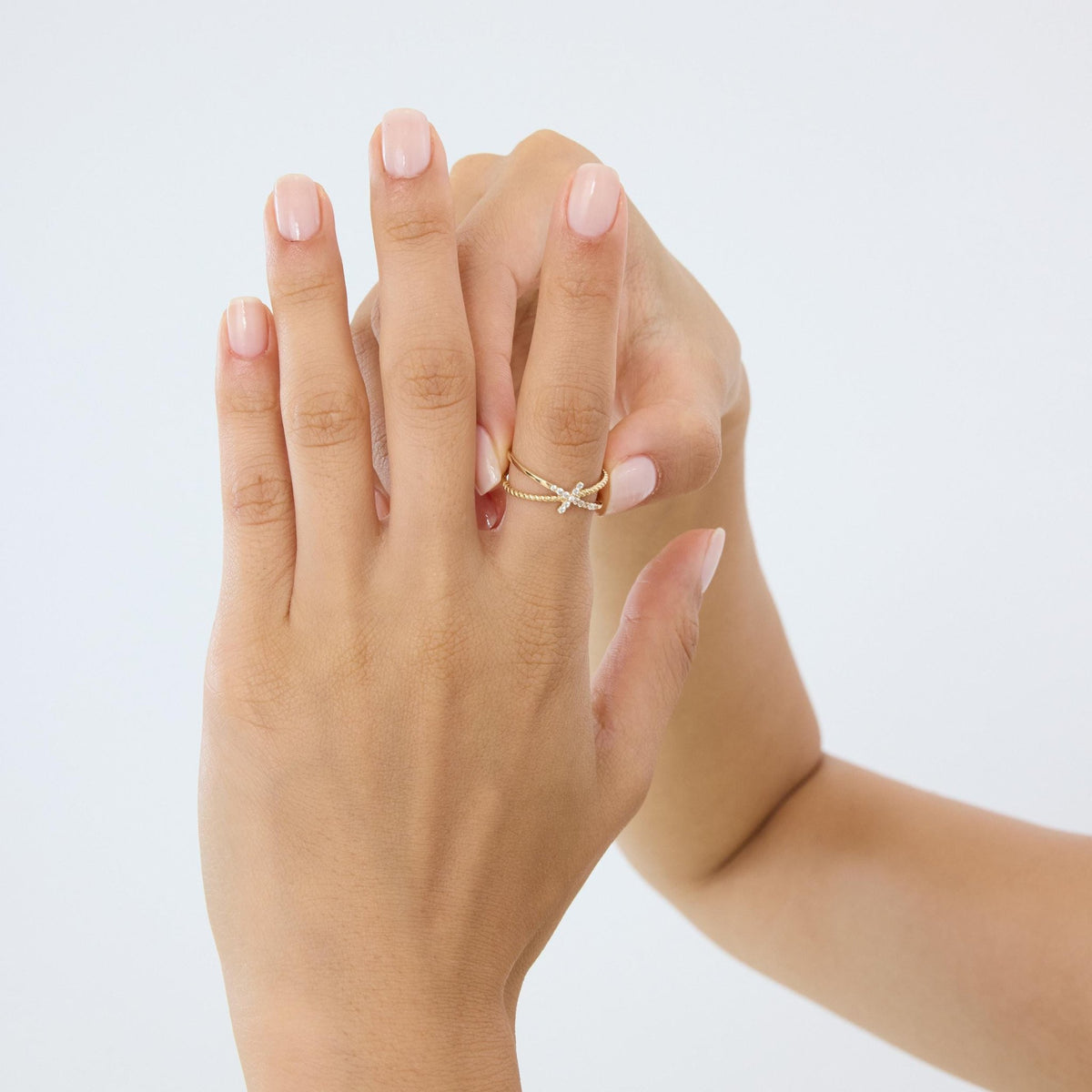 14K gold CZ cross ring worn, two hands raised against a pale grey background