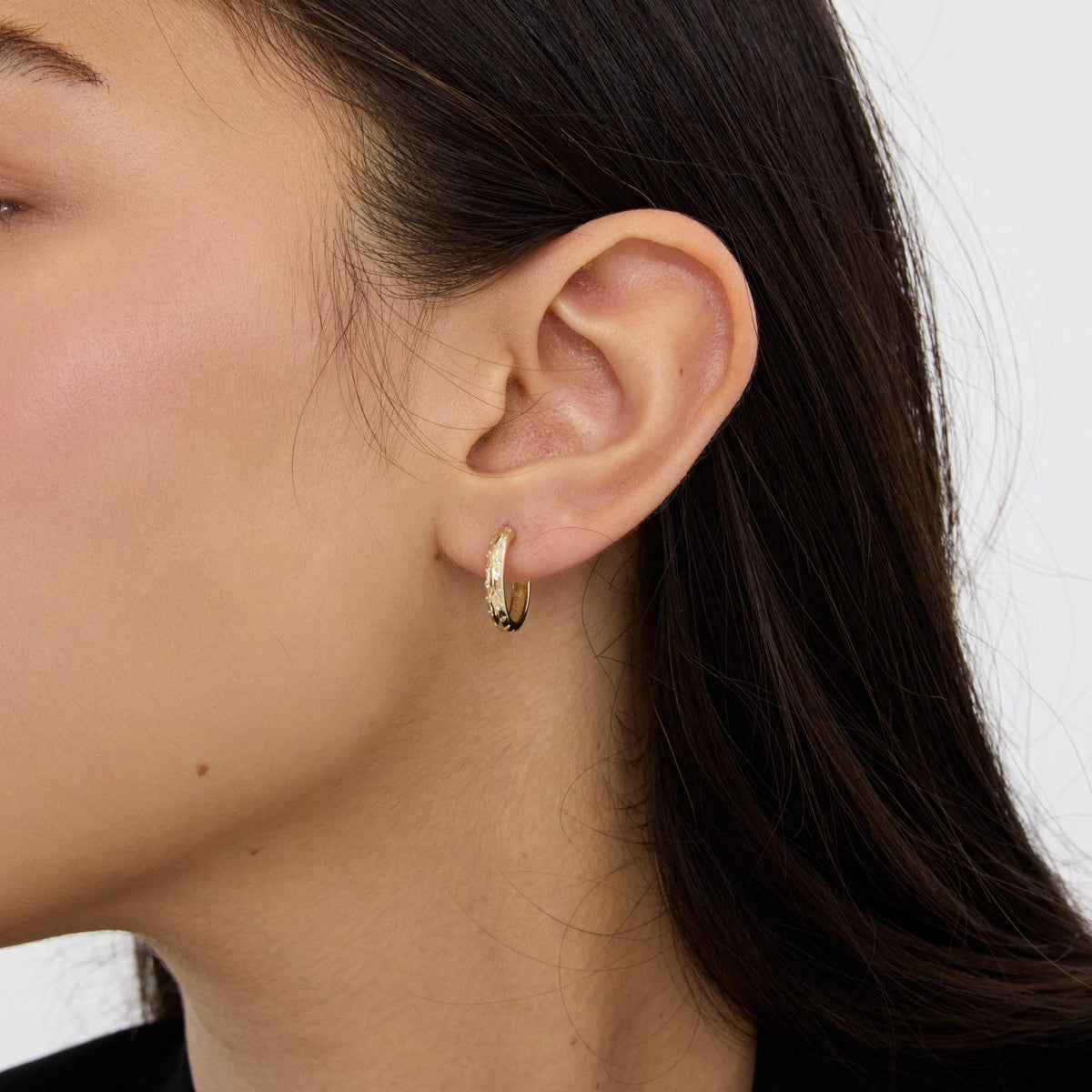 Close-up of ear wearing a 14K gold cubic zirconia hoop earring, side profile with dark hair