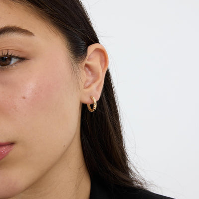 Woman wearing a small 14K gold cubic zirconia hoop earring, face half-cropped, black blazer