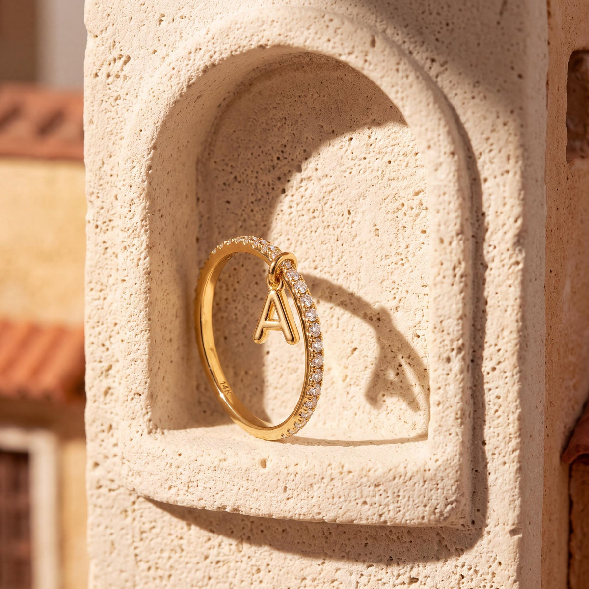 14K yellow gold dangle initial ring leaning in a rounded stone wall niche, close-up of the A charm