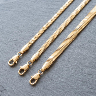 14K gold flat snake chain necklace styled on a neutral backdrop, fourth angle