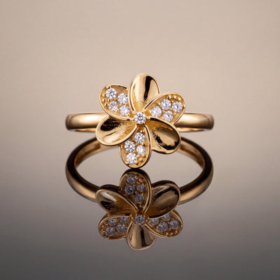 14K yellow gold flower ring standing upright on a reflective surface against a beige backdrop