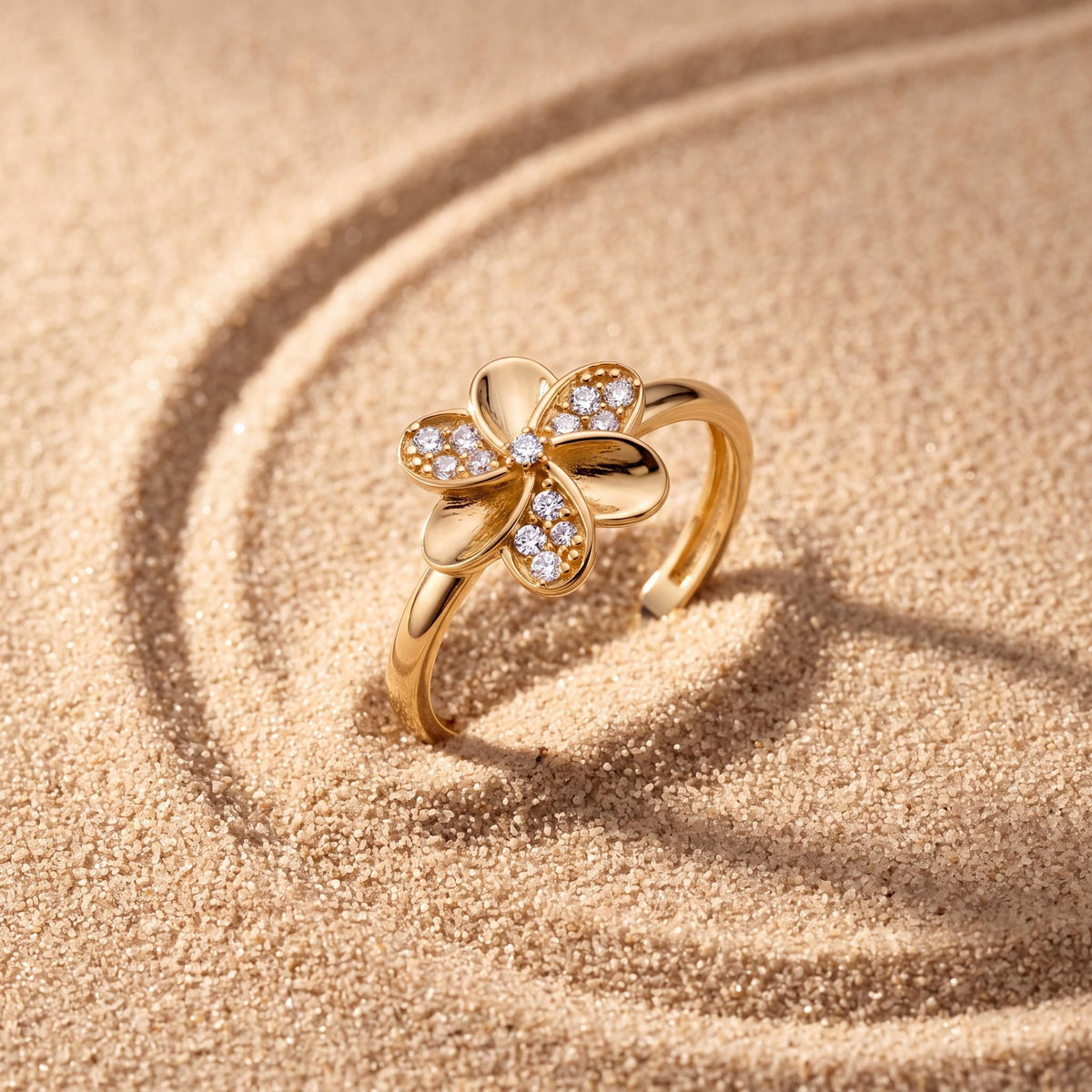 14K yellow gold flower ring set upright in rippled sand, stone-set petals facing the camera