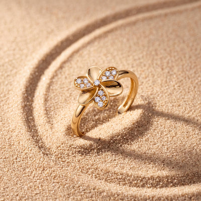 14K yellow gold flower ring set upright in rippled sand, stone-set petals facing the camera