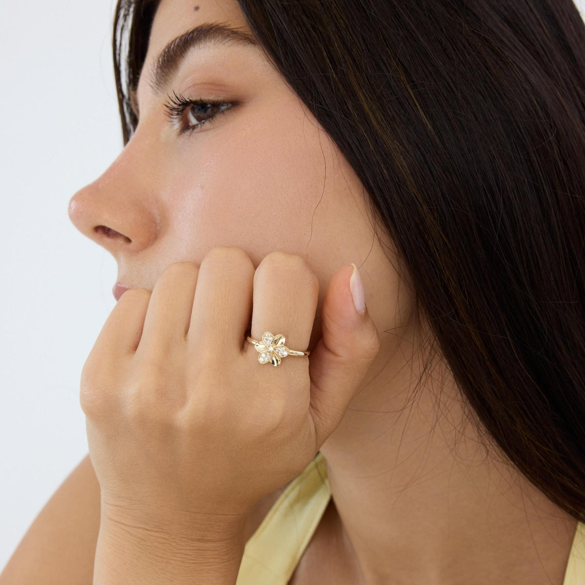 14K gold flower ring worn on a hand raised to the cheek, model seen in profile