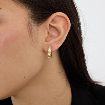 Side profile of ear wearing a 14K gold geometric huggie earring, close-up on the pyramid facets