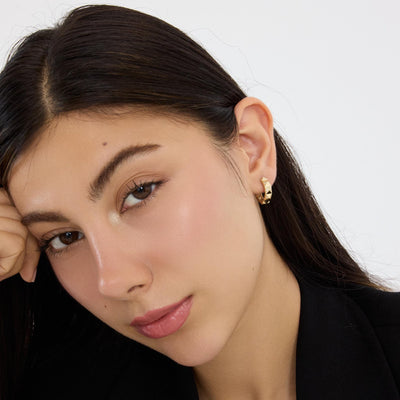 Woman resting head on hand wearing a 14K gold geometric huggie earring, small hoop seen from a distance