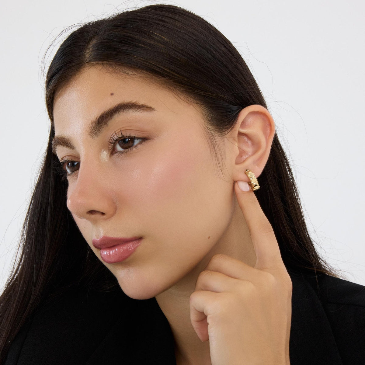 Model touching her ear with a finger to show a 14K gold geometric huggie earring