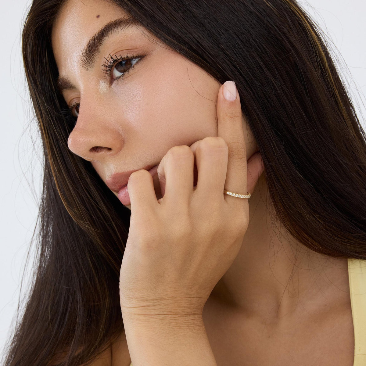 14K gold half eternity ring worn on a hand held against the cheek, model looking away