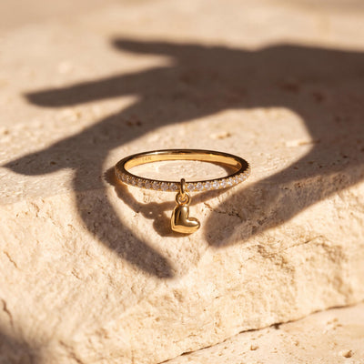 14K yellow gold heart charm ring on a limestone block with a hand's shadow falling across it