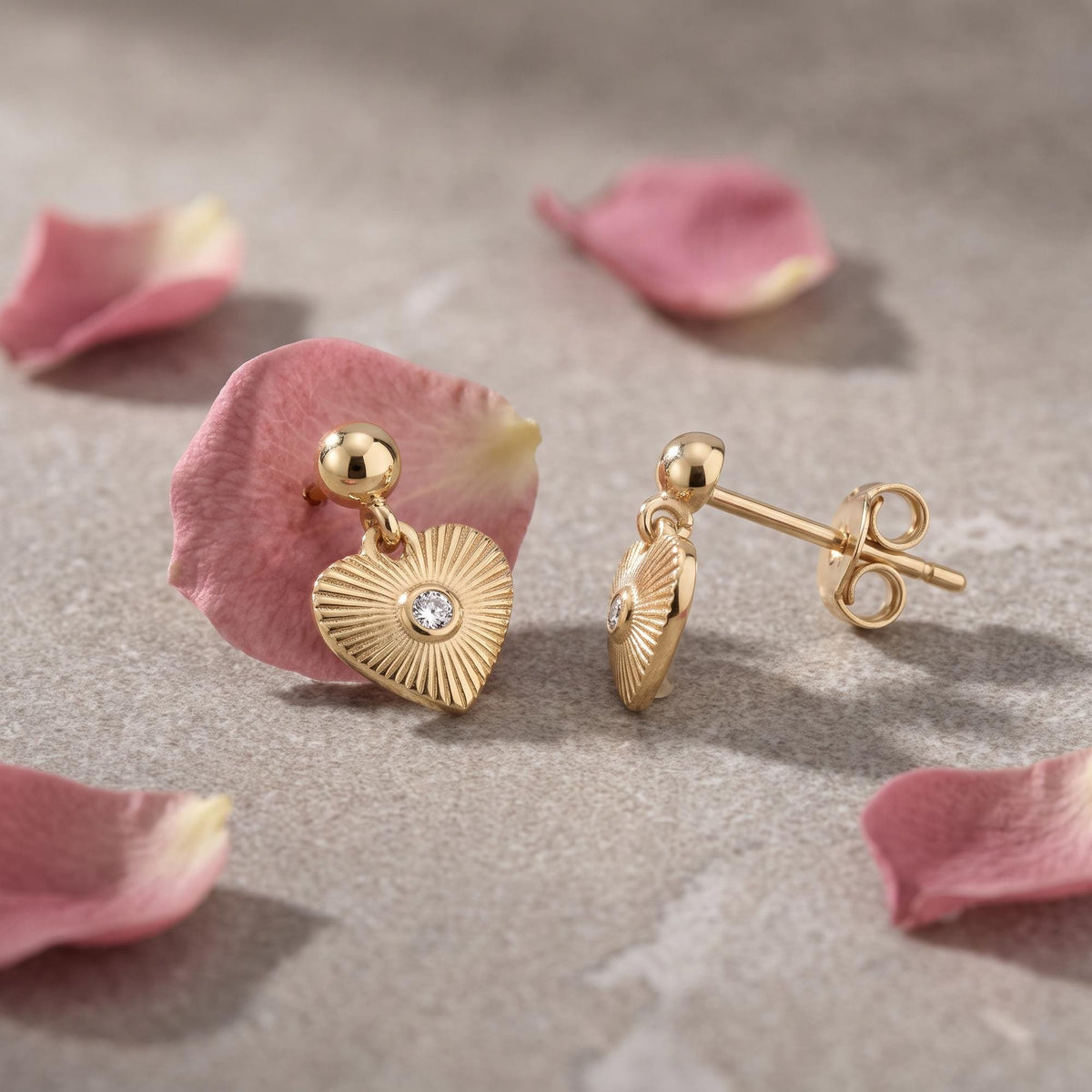 14K gold heart drop stud earrings with cubic zirconia, resting on pink rose petals, front and side view