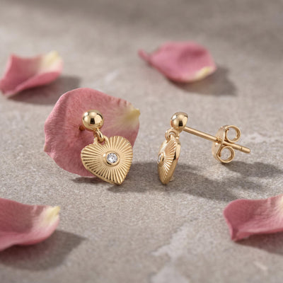 14K gold heart drop stud earrings with cubic zirconia, resting on pink rose petals, front and side view