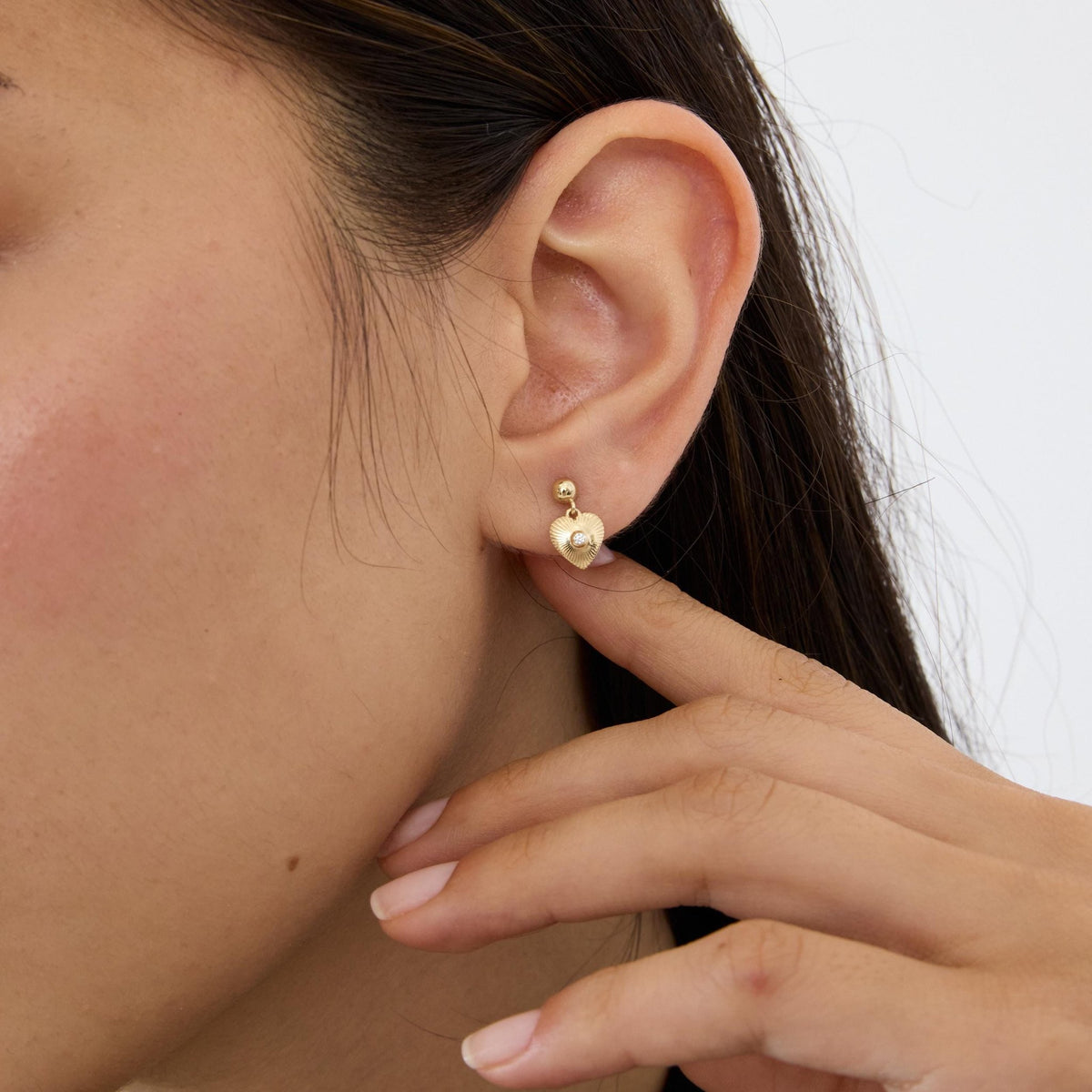 14K gold heart drop stud earring with cubic zirconia worn on the ear, one hand touching the earlobe