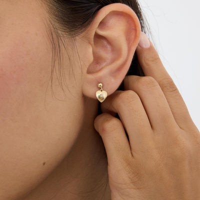 14K gold heart drop stud earring with cubic zirconia on the ear, hand raised behind the ear, close crop
