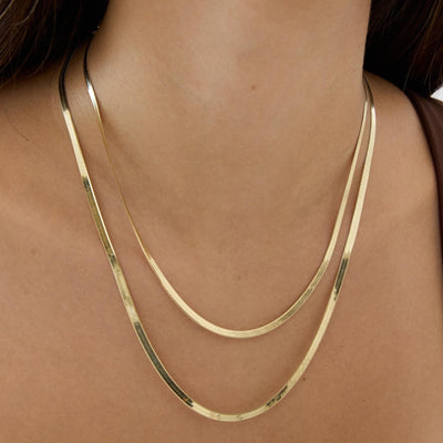 Two layered 14K yellow gold herringbone chain necklaces on a woman's neck, shorter and longer strand